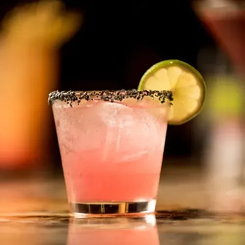 Vibrant pink cocktail with lime, ice, and dark rim.