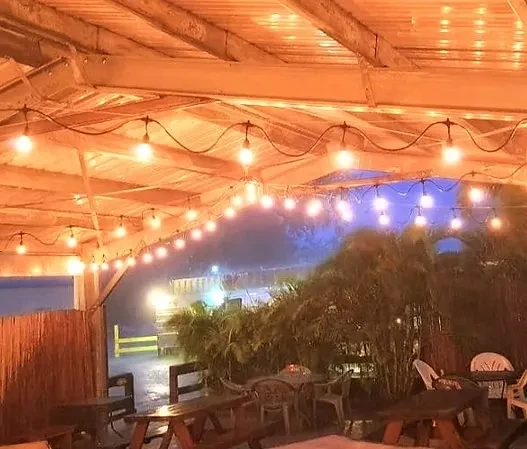 Outdoor restaurant seating area illuminated by warm string lights at night.