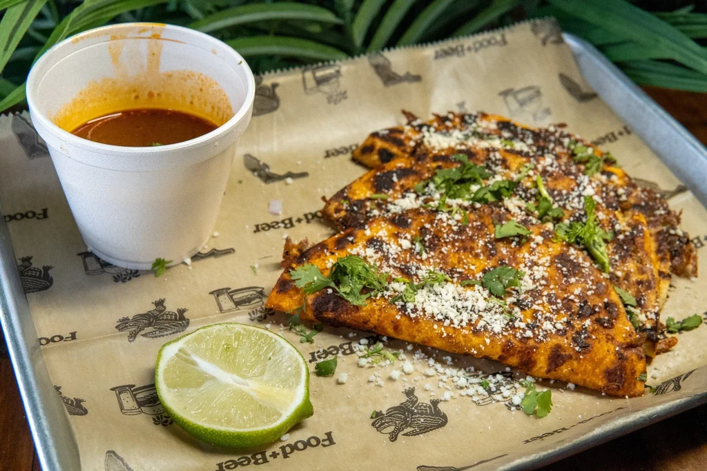 Three birria tacos with cheese, cilantro, consommé, and lime.