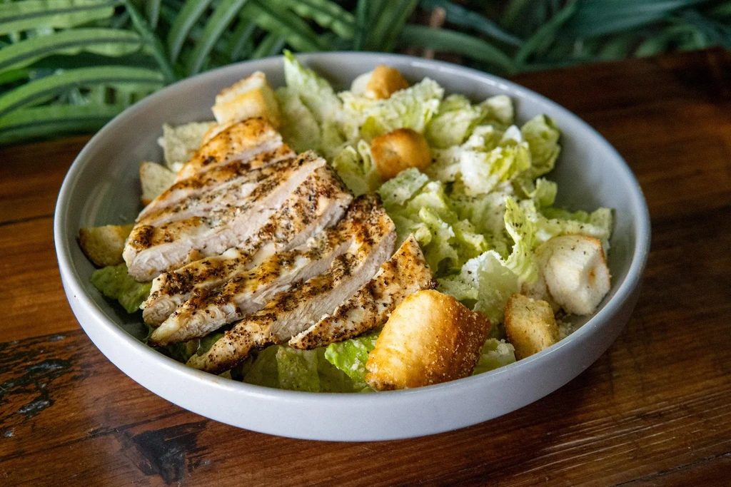 Close-up grilled chicken Caesar salad with cheese, croutons in a bowl.