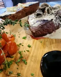 Close-up: Cooked meat, creamy sauce, red tomatoes, and green herbs on wood.