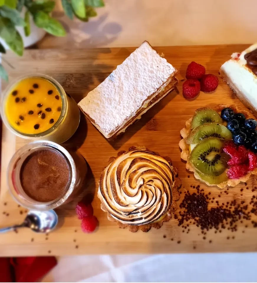 Wooden board displaying various desserts: tarts, mille-feuille, mousse, cheesecake.