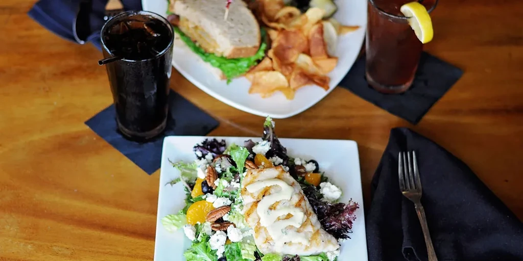 Top-down: grilled chicken salad, sandwich, chips, and two drinks.