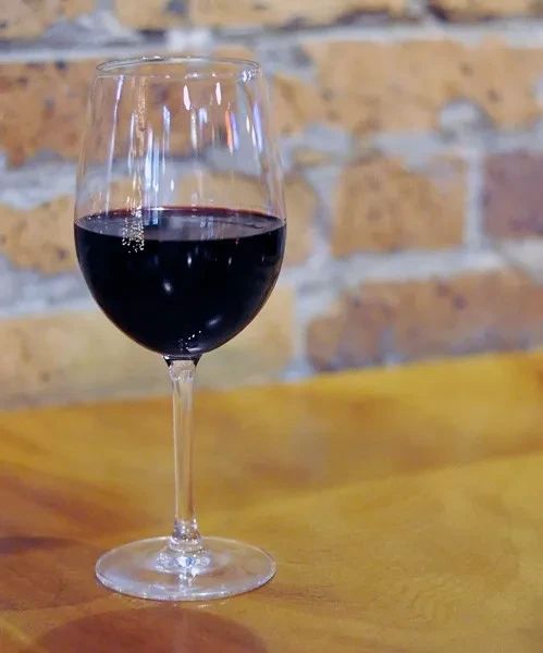 Wine glass with red wine on a wooden table, blurred brick background.