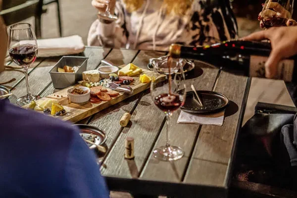 Wooden charcuterie board with cheeses, meats, berries, and red wine pouring.