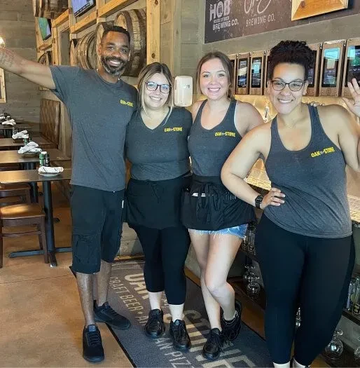 Four smiling staff in uniform at Oak & Stone Brewery.