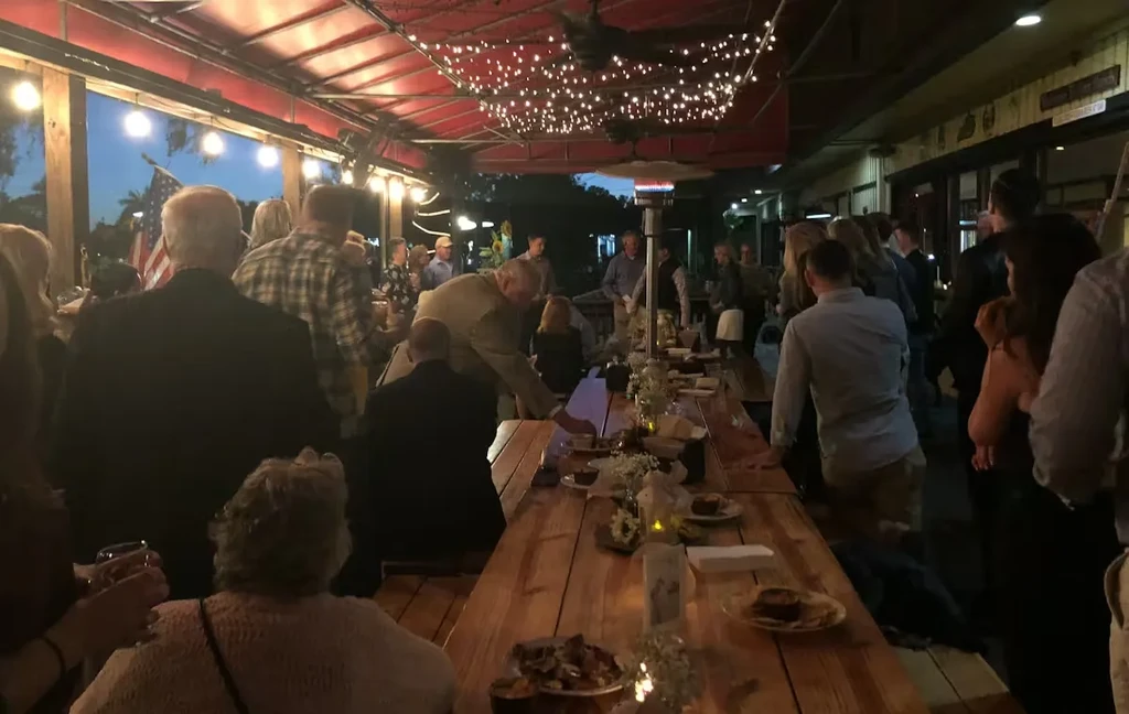 Lively evening patio with string lights, rustic tables, and socializing people.