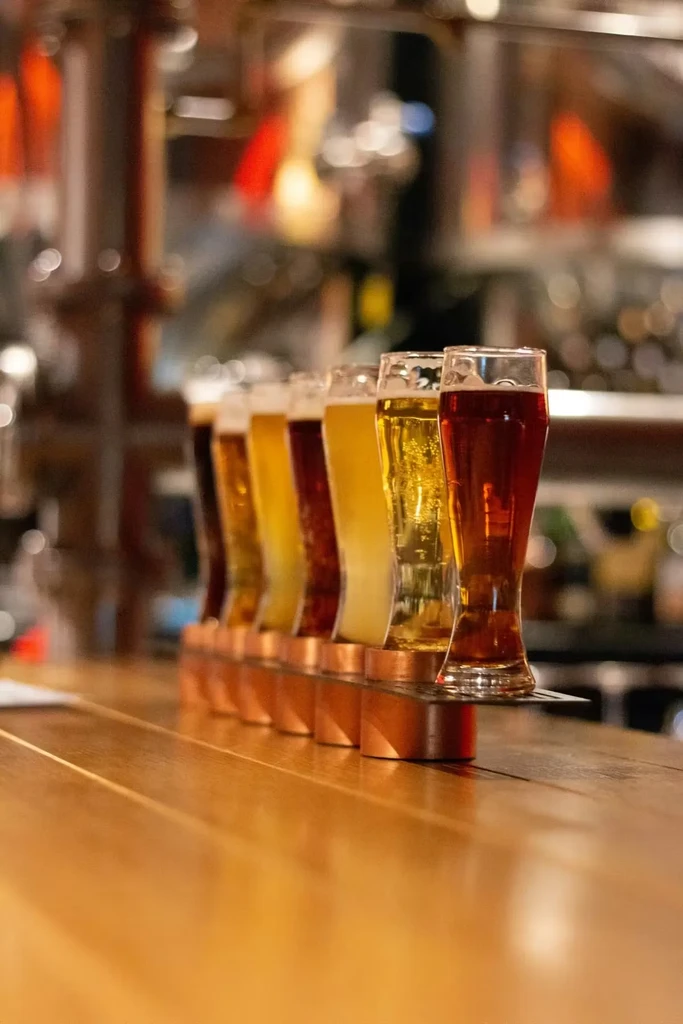 Six beers in a copper flight holder on a wooden bar.