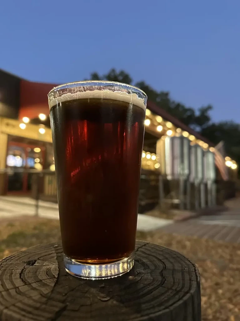 Dark amber beer with foam on rustic wood, outdoor brewery.