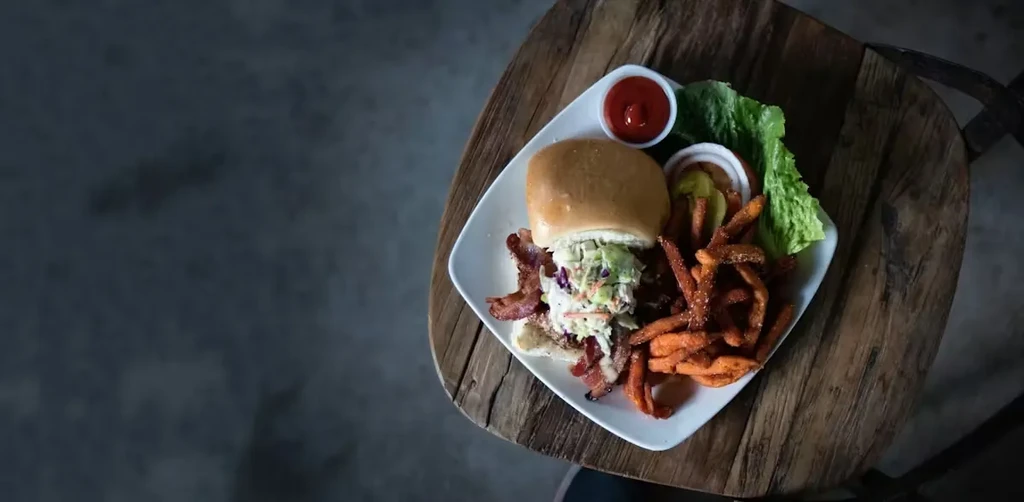 Pulled pork sandwich, bacon, coleslaw, sweet potato fries on table.