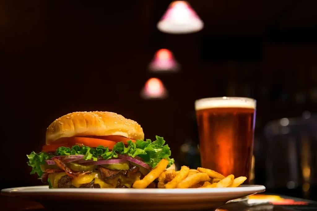Close-up of a stacked cheeseburger, golden fries, and a frothy beer.