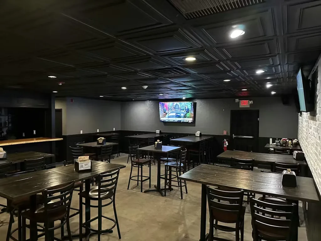 Empty, modern restaurant interior with dark walls and wooden furnishings.