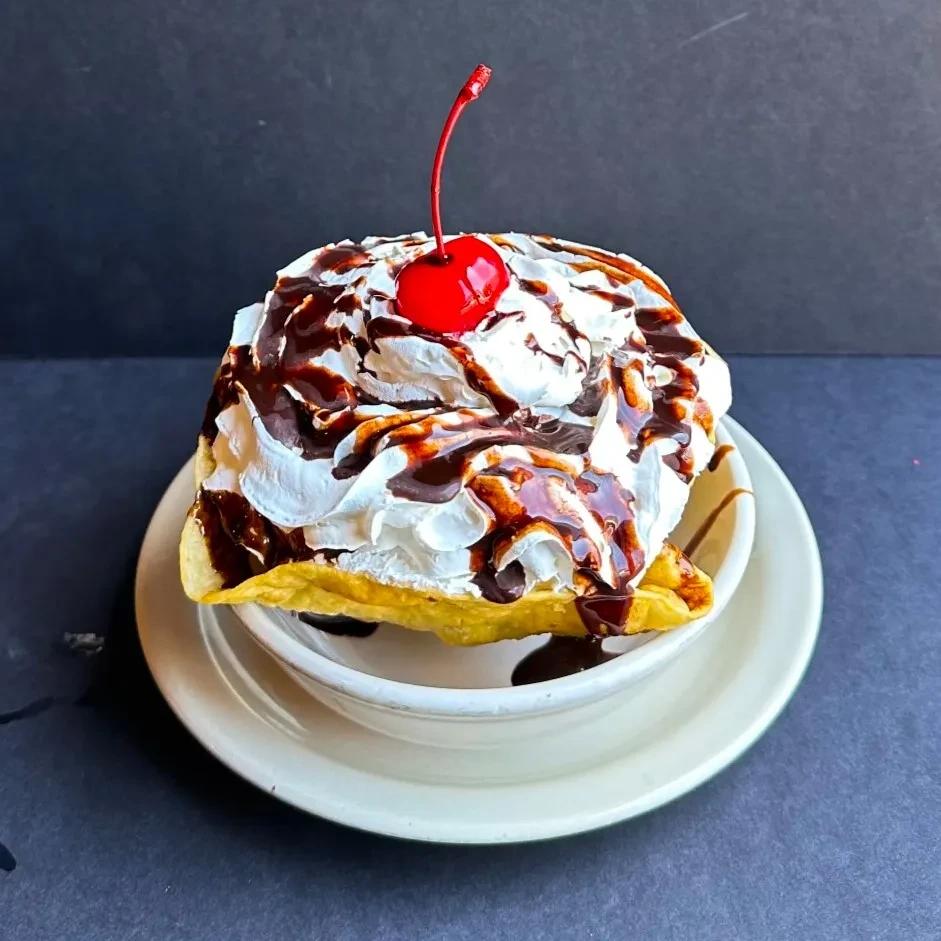 Waffle with whipped cream, dark chocolate sauce, and a maraschino cherry.