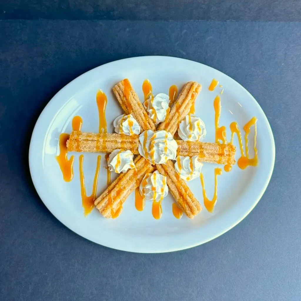 Overhead view of cinnamon sugar churros with whipped cream and caramel.