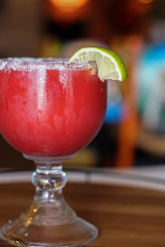 Red frozen drink in a goblet with sugared rim and lime slice.