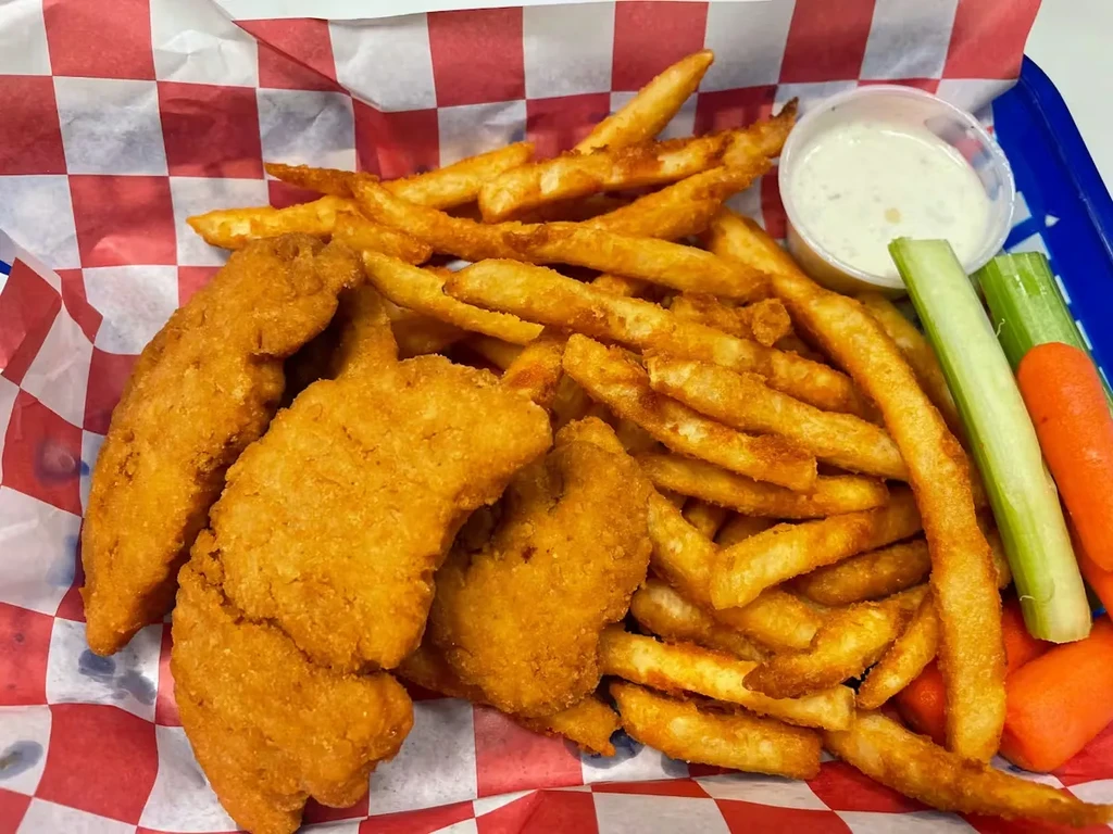 Close-up of fried chicken tenders, fries, dipping sauce, carrots, and celery.