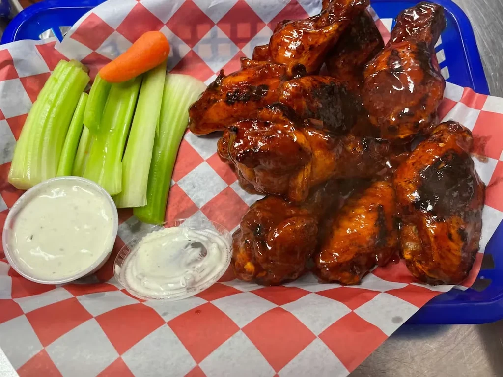 Basket of sauced chicken wings, celery, carrot, and two dipping sauces.