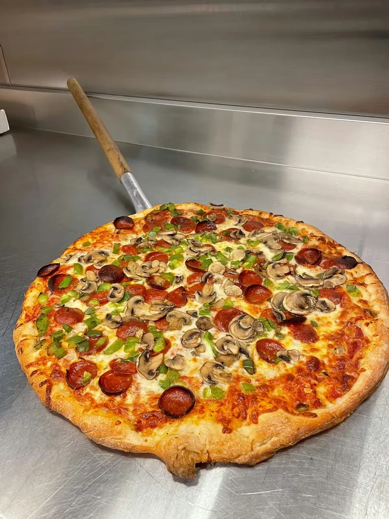 Freshly baked pizza with pepperoni, mushrooms, peppers on stainless steel.