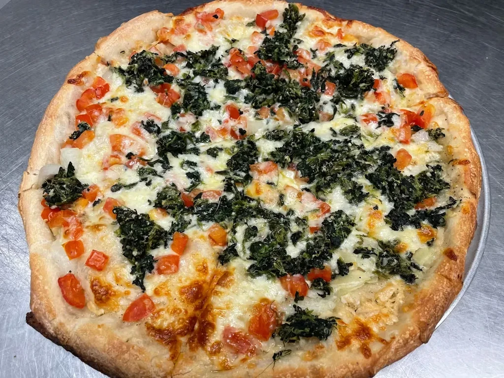 Round pizza with cheese, tomatoes, and greens on a metallic surface.