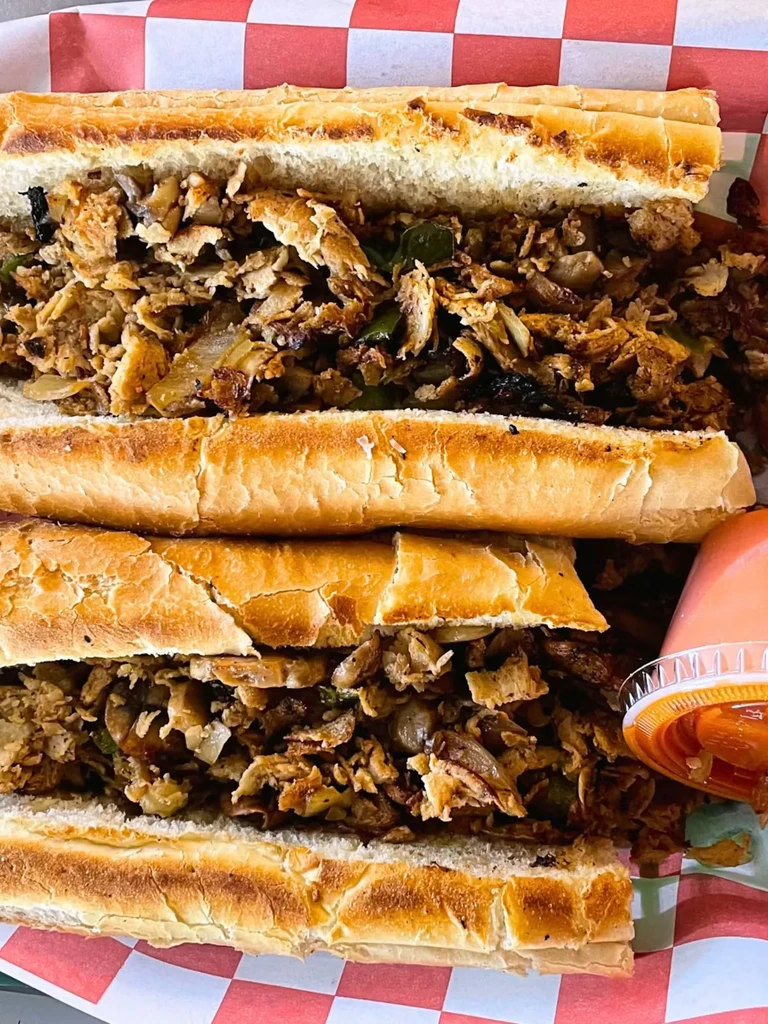 Two large meat and vegetable hoagies in a deli basket, with sauce.