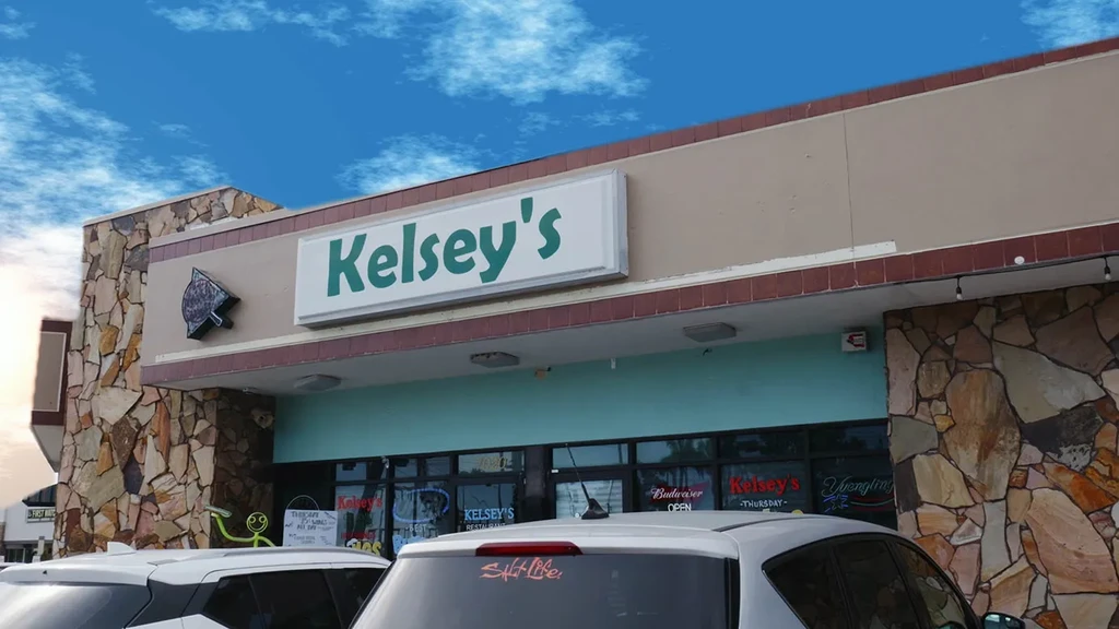 Kelsey's restaurant exterior with stone facade, turquoise band, and parked cars.