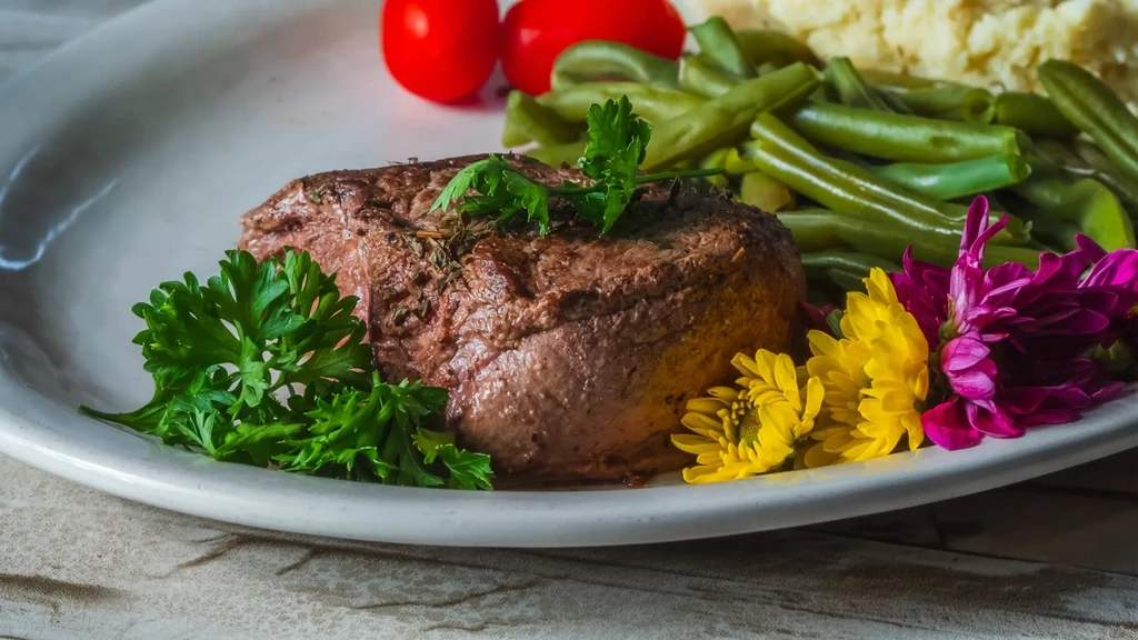 Plated steak with herbs, colorful flowers, parsley, and vegetable sides.