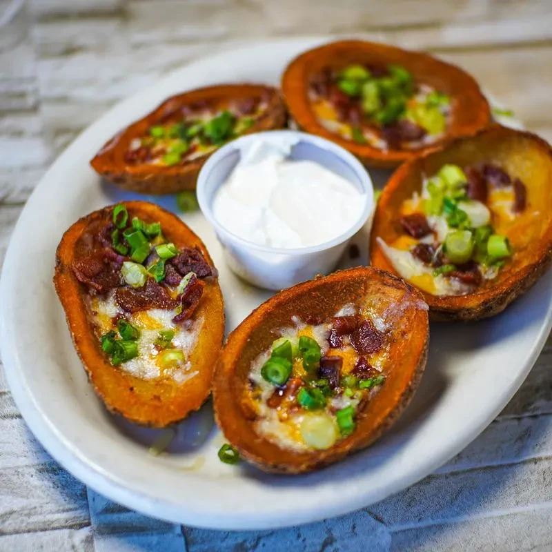 Plate of golden potato skins with cheese, bacon, green onions, and dip.