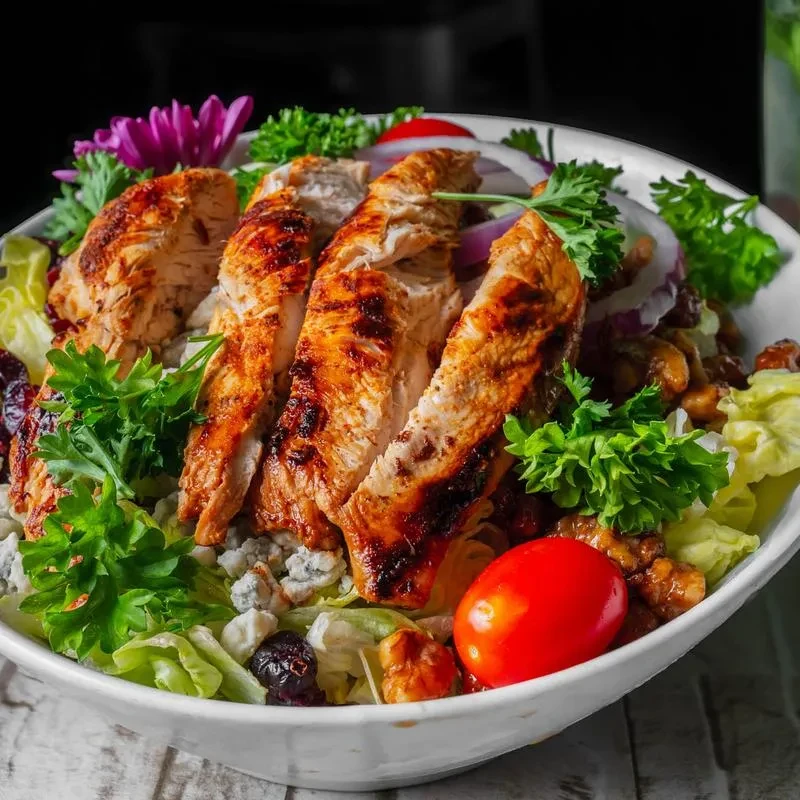 Close-up of grilled chicken salad with lettuce, tomatoes, cranberries, blue cheese, walnuts.