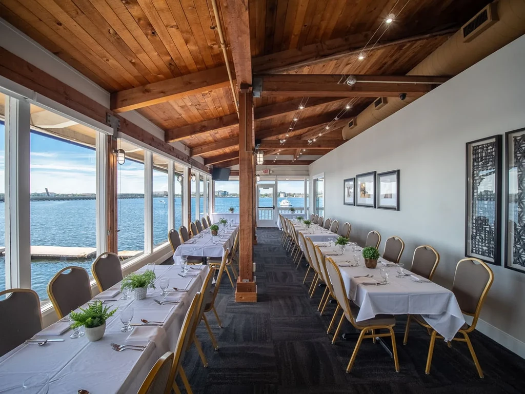 Waterfront restaurant dining room with vaulted wooden ceiling and set tables.