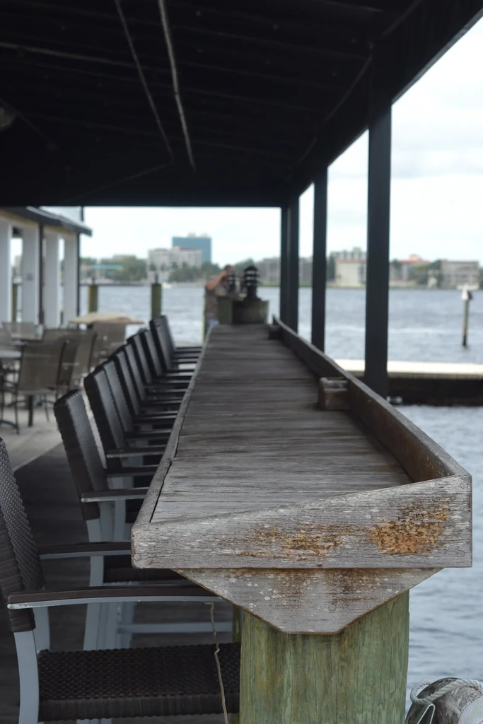 Rustic wooden bar counter and stools overlooking a waterfront.
