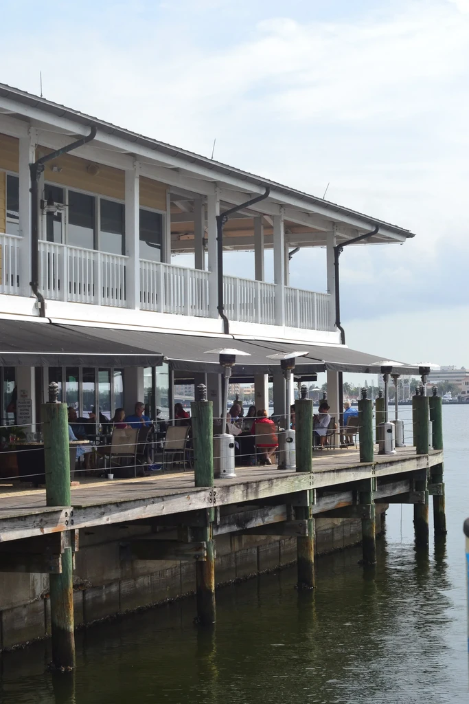 Waterfront restaurant on pier; people dine on shaded patio.