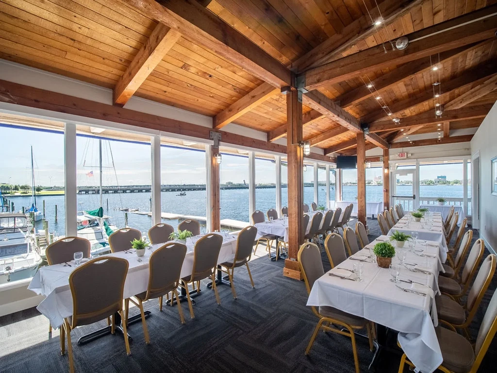 Bright dining room with white tables, vaulted wood ceiling, marina view.