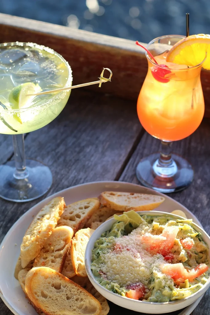 Colorful cocktails and appetizers on a weathered wooden table outdoors.