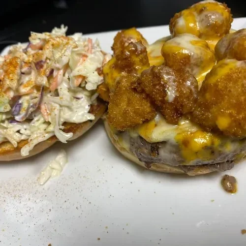 Coleslaw on a bun beside a cheeseburger topped with fried shrimp.