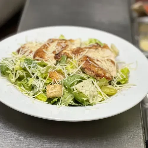 Close-up of grilled chicken Caesar salad on a white plate.