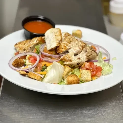 Grilled chicken salad with greens, cheese, croutons, and side dressing.
