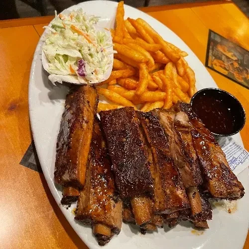 Close-up of glazed ribs, golden fries, coleslaw, and barbecue sauce.