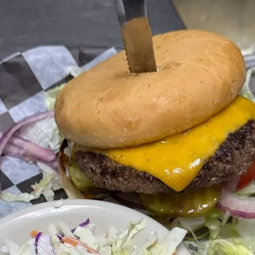 Cheeseburger with melted cheese, held by a knife, served with coleslaw.