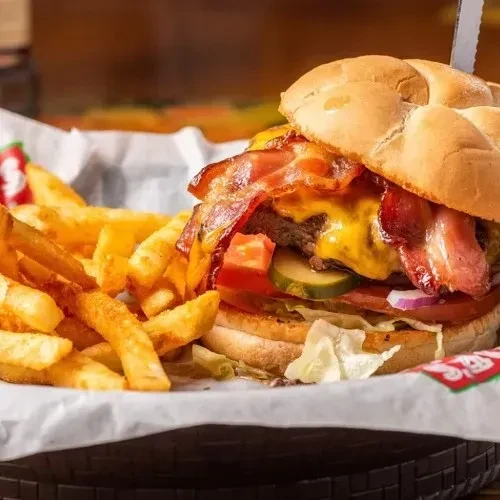 Bacon cheeseburger, held by skewer, and fries in a dark basket.