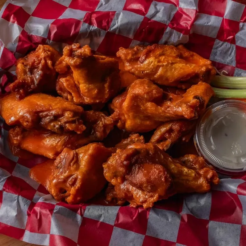 Glossy buffalo wings in a checkered basket with dip and celery.