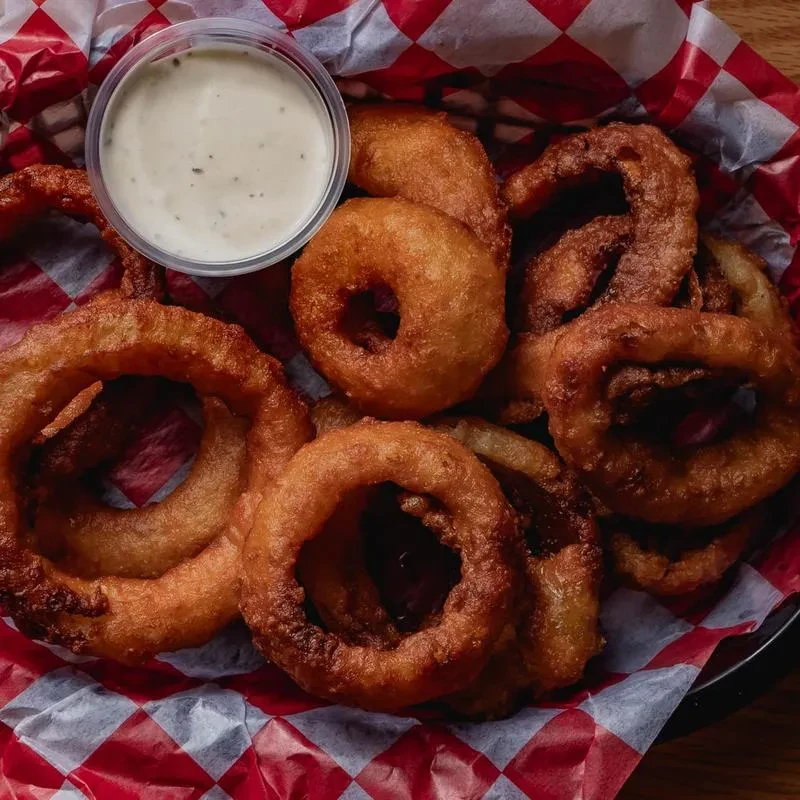 Crispy fried onion rings in a checkered basket with dipping sauce.