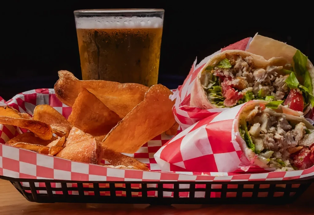 Chicken wraps, potato chips, and beer served in a lined basket.