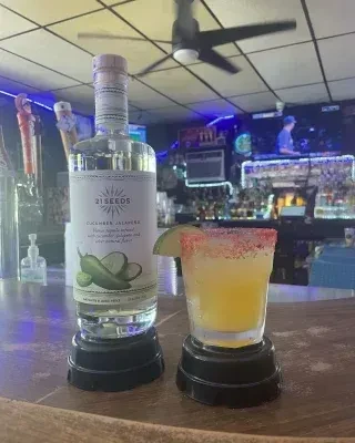 Cucumber jalapeño tequila and red-rimmed yellow cocktail on bar.