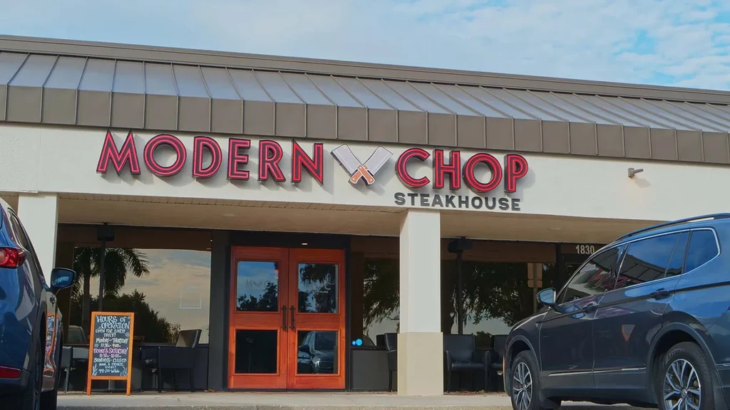 Exterior of MODERN CHOP Steakhouse, glowing red sign, parked cars.