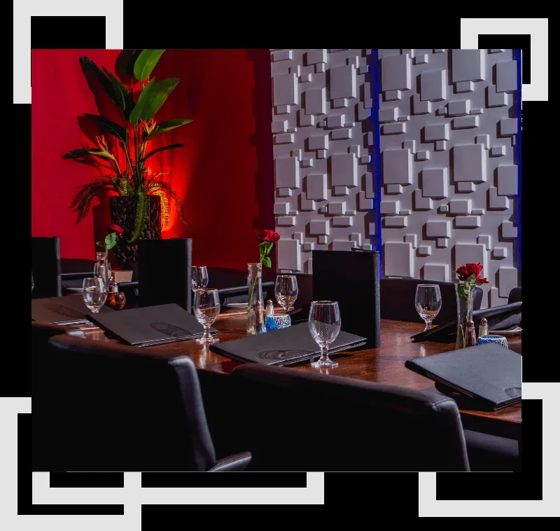 Long dark restaurant table set with red roses, red and textured walls.