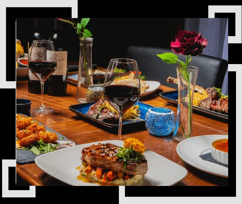 Dining table with steak, red wine, fried food, and flowers.