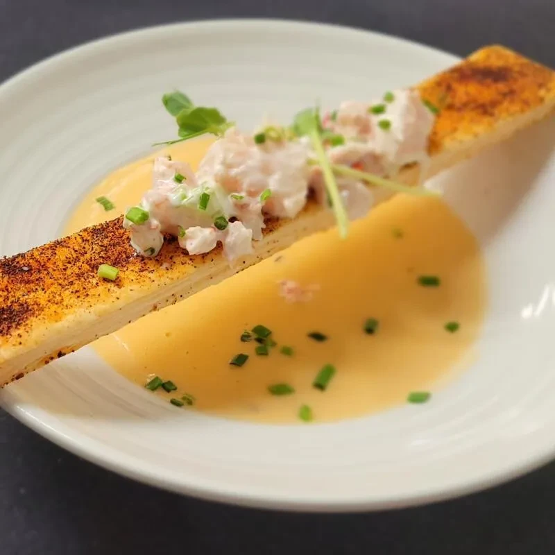 Rectangular terrine topped with seafood, chives, and yellow sauce.