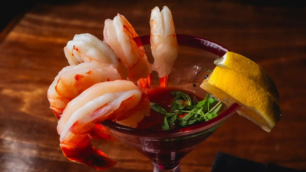 Peeled shrimp cocktail in martini glass with lemon and sauce.