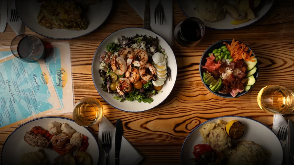 Rustic wooden table with shrimp salad, poke, drinks, and menu.