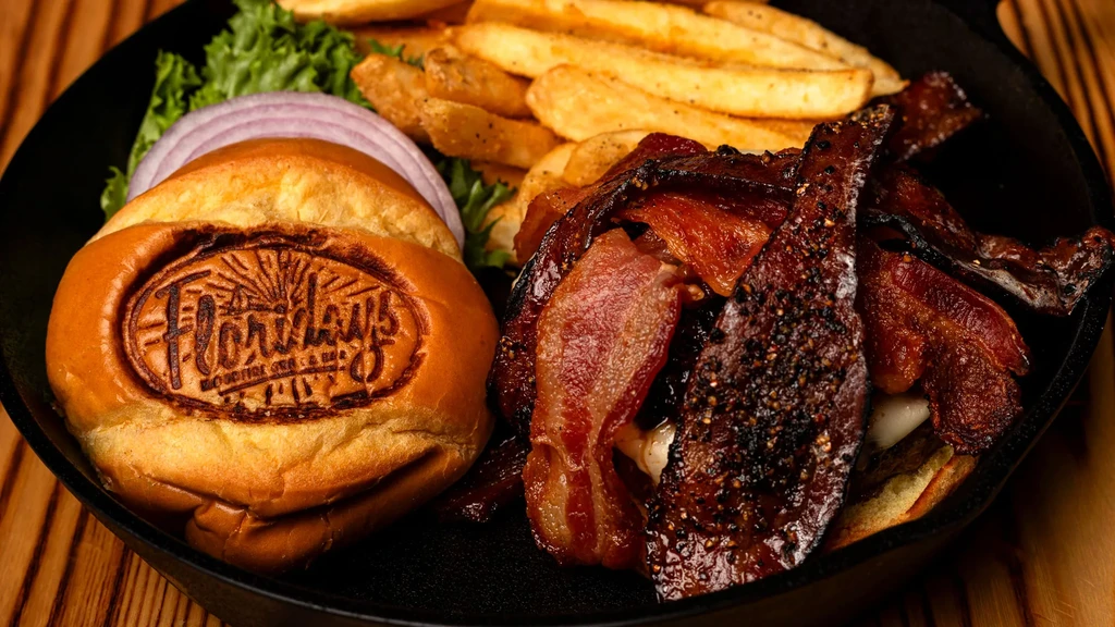 Overhead view of a Floridays burger, fries, and crispy bacon in a skillet.
